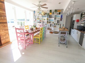 A bright kitchen with white cabinets, a wooden dining table, and colorful chairs.