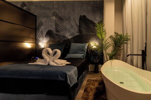 A modern bedroom with a large bed, a bathtub, and a wall with a leaf pattern.