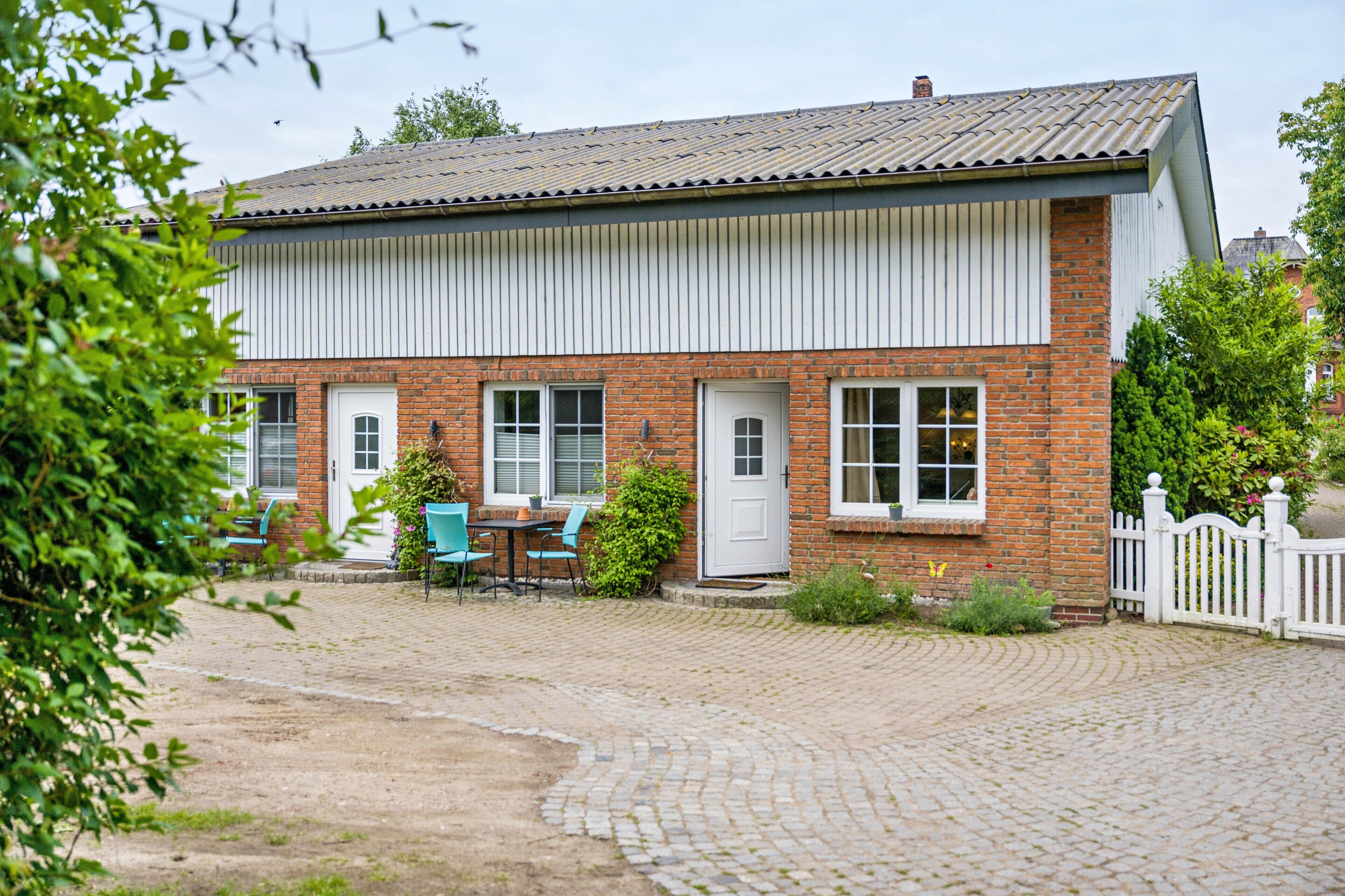 A two-story brick building with a white exterior, a paved driveway, and a white picket fence.