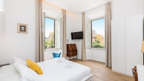 Habitación de hotel con cama, televisi ón, silla y ventanas amplias con vista a la ciudad.