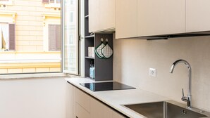 Una cocina moderna con estufa integrada, un lavamanos y un ventanal con vista a un edificio amarillo.
