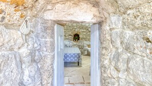 Ein Blick ins Innere eines Zimmers mit Steinwänden, einem Bett, einem Tisch und einem Stuhl.
