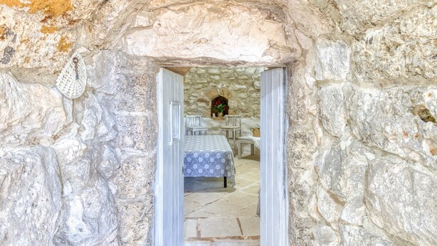 Vista del interior de una habitación con paredes de piedra, una cama, una mesa y una silla.