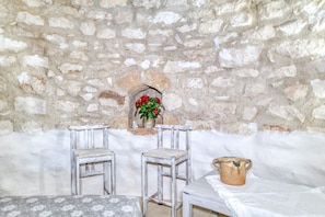 A stone-walled room with two wooden chairs, a table, and a vase with flowers.