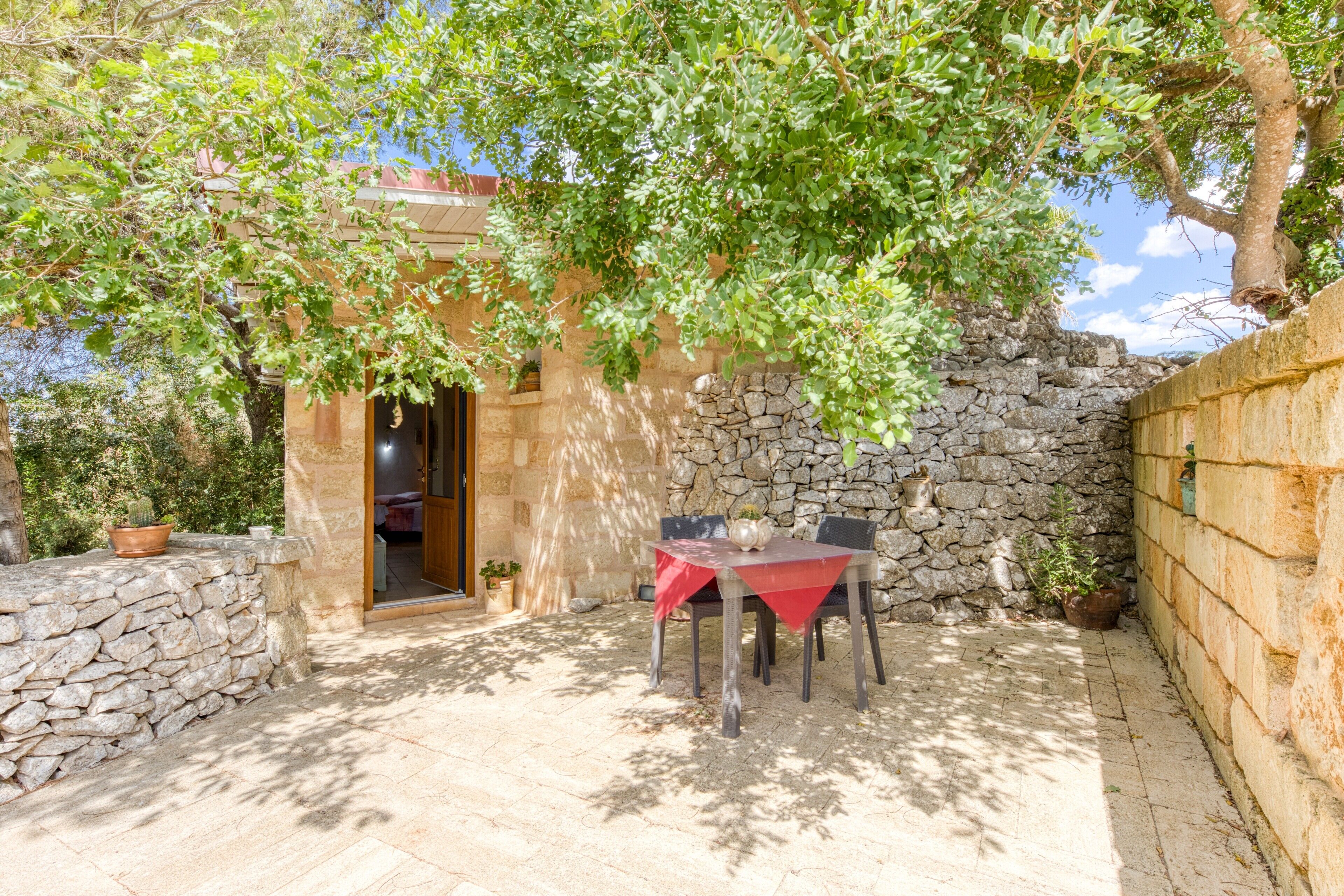 A stone-walled outdoor area with a table and chairs, a potted plant, and a doorway leading to a room.