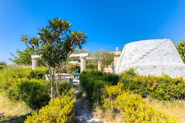 A garden pathway leading to a building with a white facade and a large white rock.