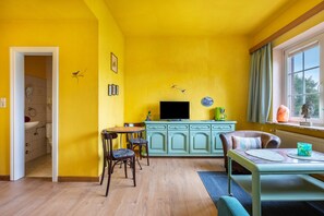Une pièce aux murs jaunes, avec un plancher en bois, une table à manger entourée de chaises, un téléviseur et un meuble.