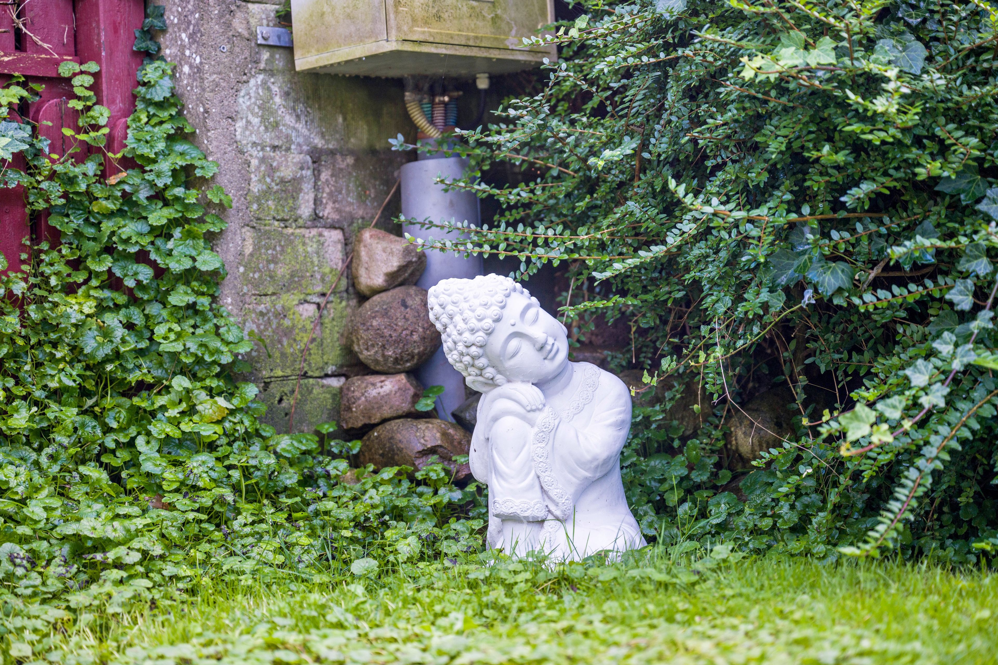 Une statue blanche représentant une figure, placée dans un jardin verdoyant, avec une structure rouge en arrière-plan.