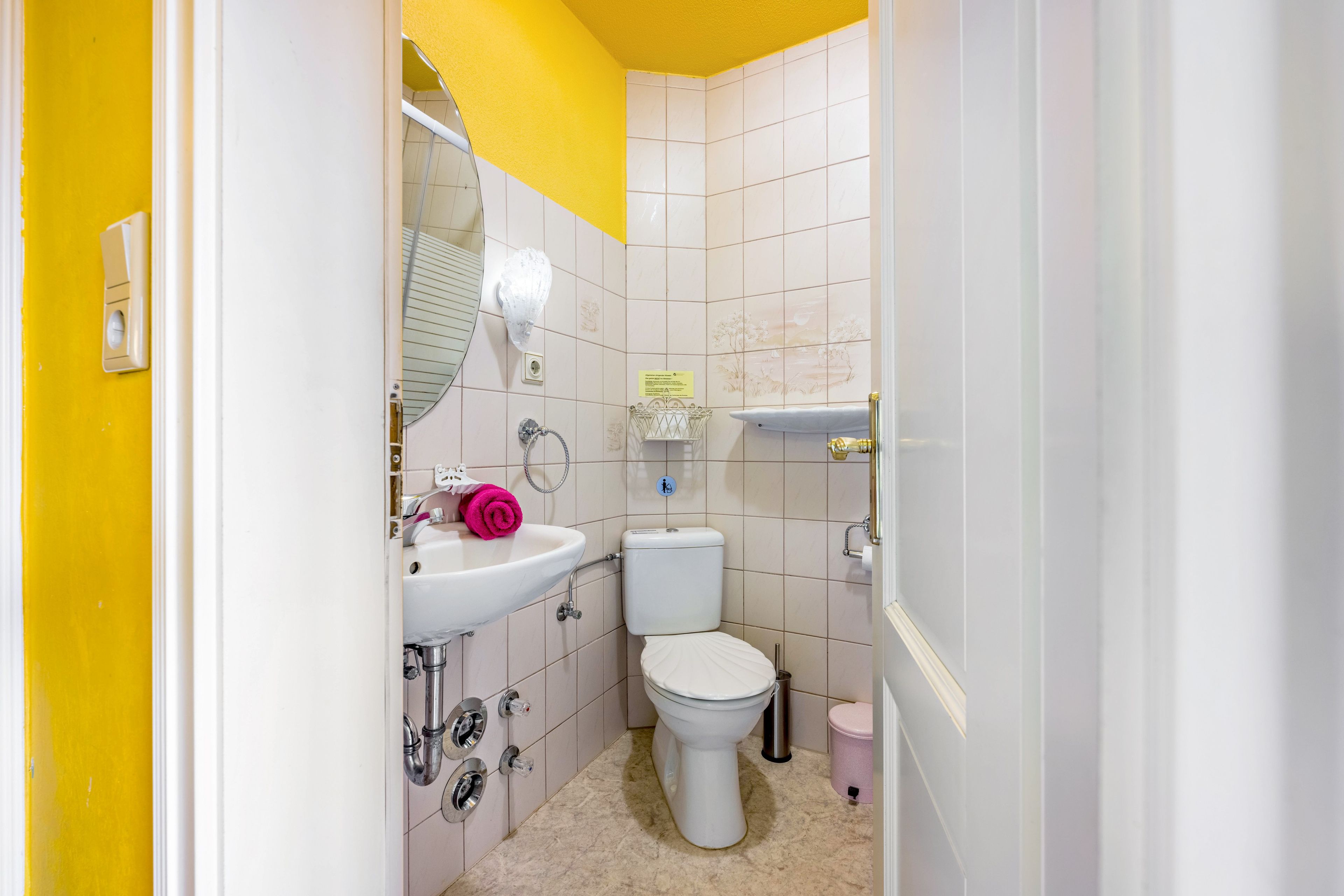 A bathroom with a white sink, toilet, and shower area, with yellow walls and a tiled floor.