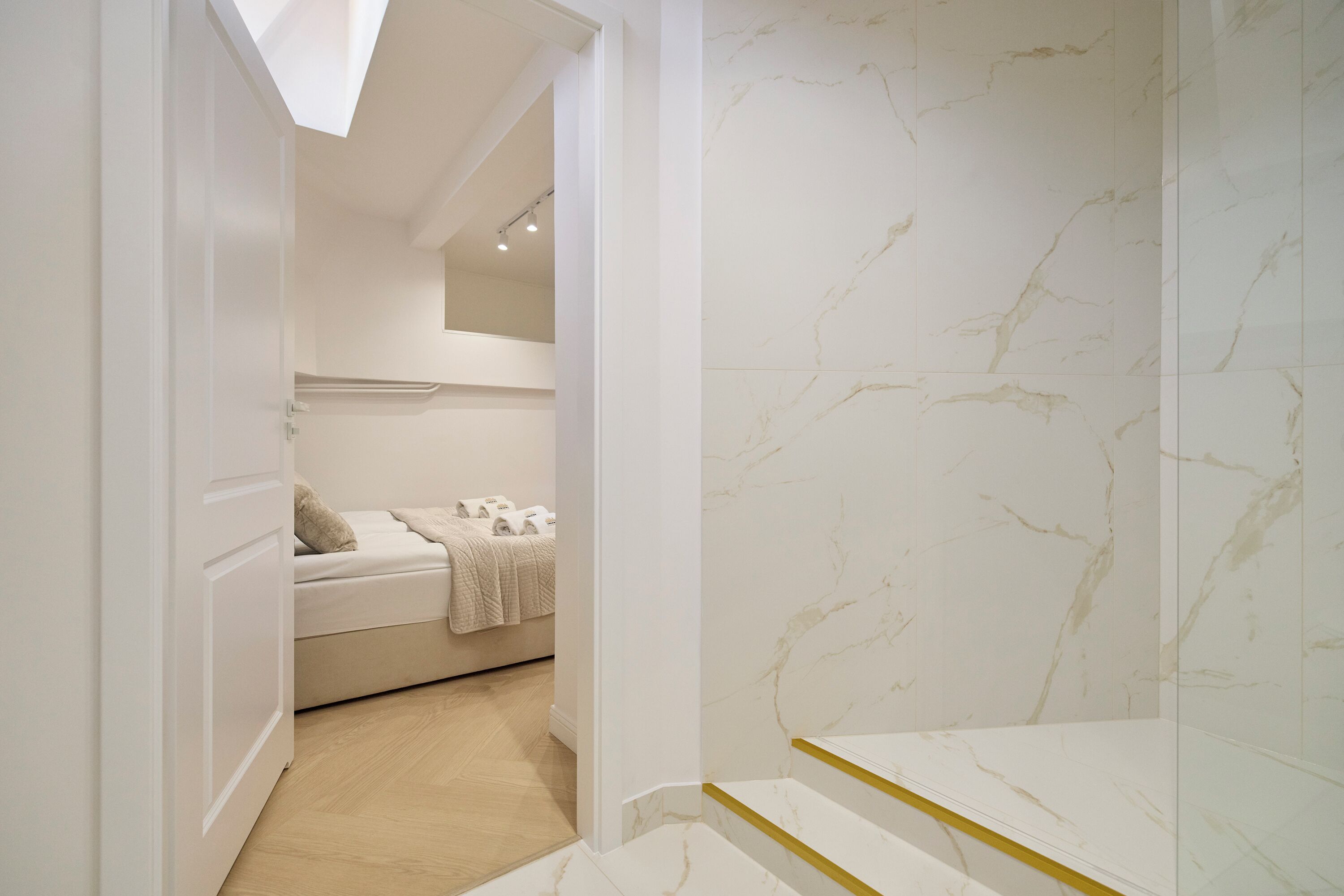 A modern bathroom with marble walls, a white bathtub, and a wooden staircase.