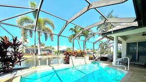 Una piscina con cerramiento de vidrio, palmeras y sillones de descanso.