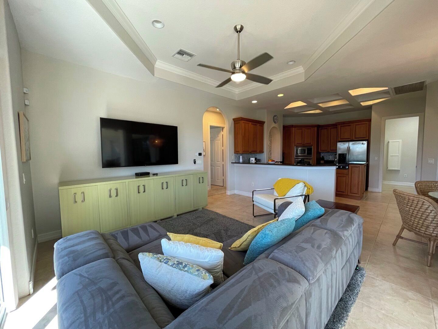 A modern living room with a large gray sectional sofa, a flat-screen TV, and a ceiling fan.