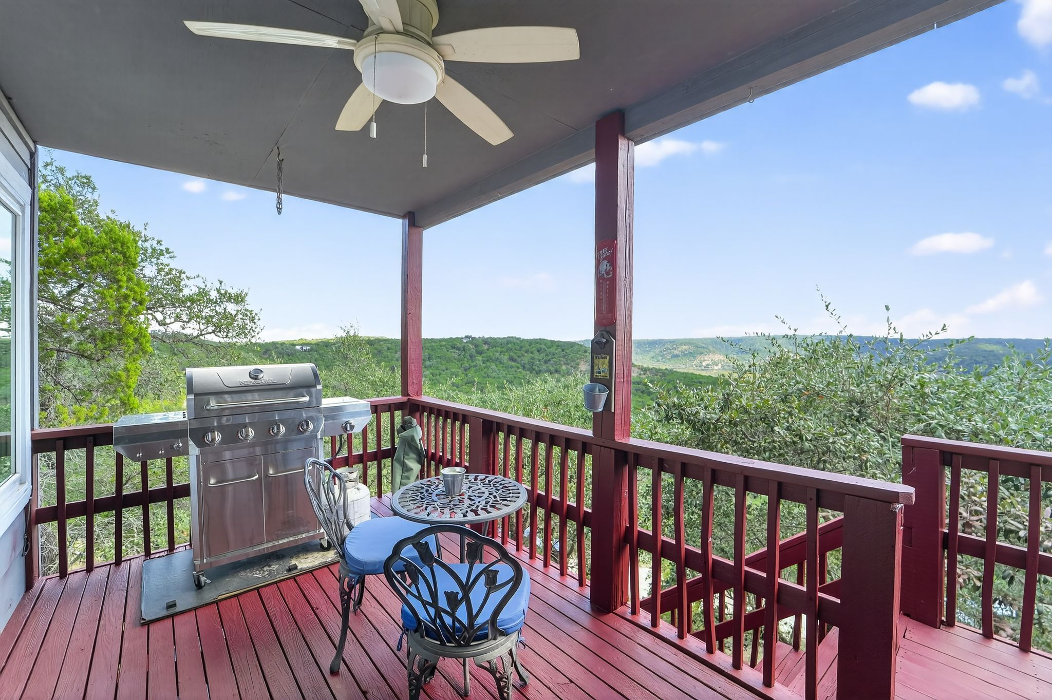A covered outdoor area with a grill, a table, and chairs, overlooking a green landscape.