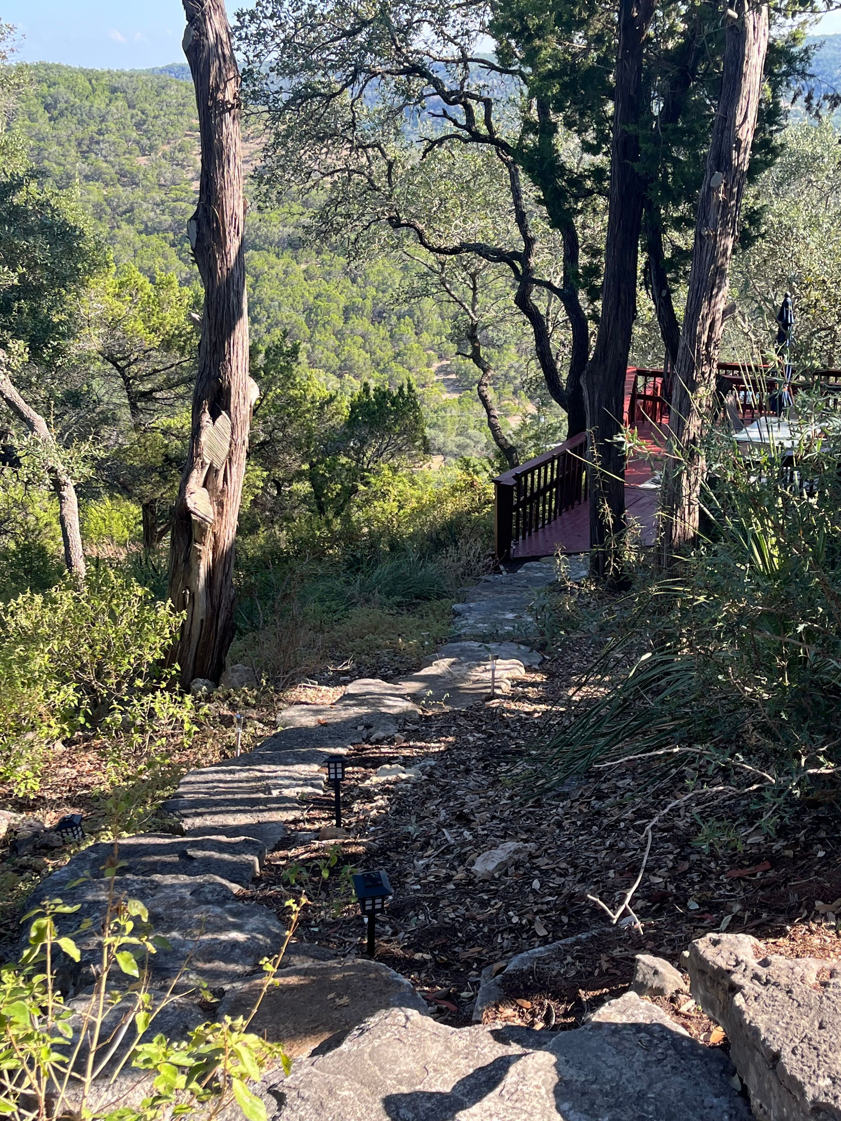 A stone pathway leading through a wooded area with a wooden bridge over a small stream.