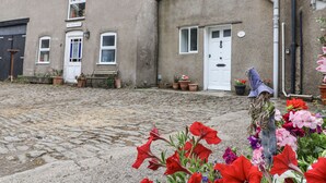 Un edificio de piedra tradicional con un patio adoquinado, una banca y plantas en macetas.
