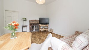 Una sala de estar con una mesa de madera, un sofá, un televisor, una chimenea y un jarrón con flores.