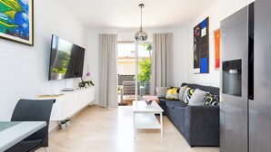 A modern living room with a flat-screen TV, a sofa, a dining table, and a kitchen area with a refrigerator. - Home2Book Relaxing Stay with Terrace & Pool (Puerto Santiago)