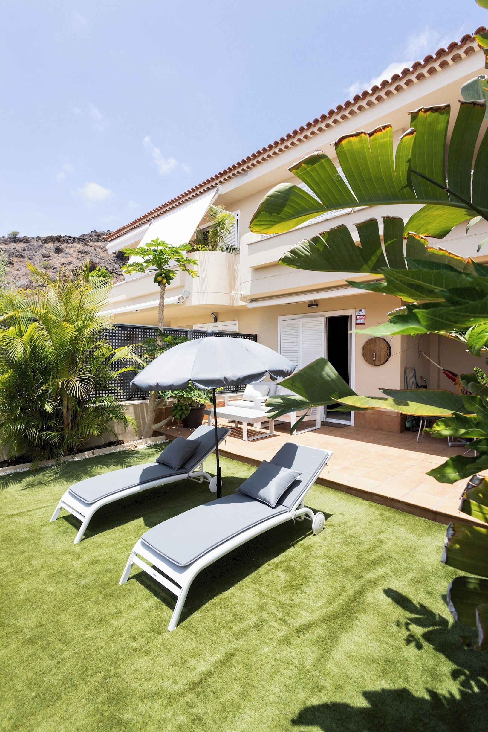 A villa with a patio, two lounge chairs, a table, and an umbrella.