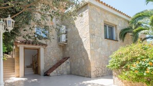 A stone building with a tiled courtyard, a staircase, and a small garden area with orange flowers. - Th01 Villa en Salou 4 Dorm 4 ba os Barbacoa (Salou)