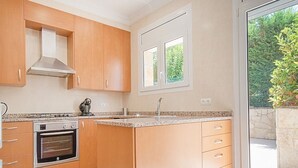 A modern kitchen with wooden cabinets, a built-in oven, and a large window providing a view of greenery outside. - Th01 Villa en Salou 4 Dorm 4 ba os Barbacoa (Salou)