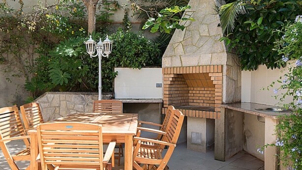 An outdoor patio with a stone barbecue grill, wooden dining table and chairs, and a lamp post. - Th01 Villa en Salou 4 Dorm 4 ba os Barbacoa (Salou)