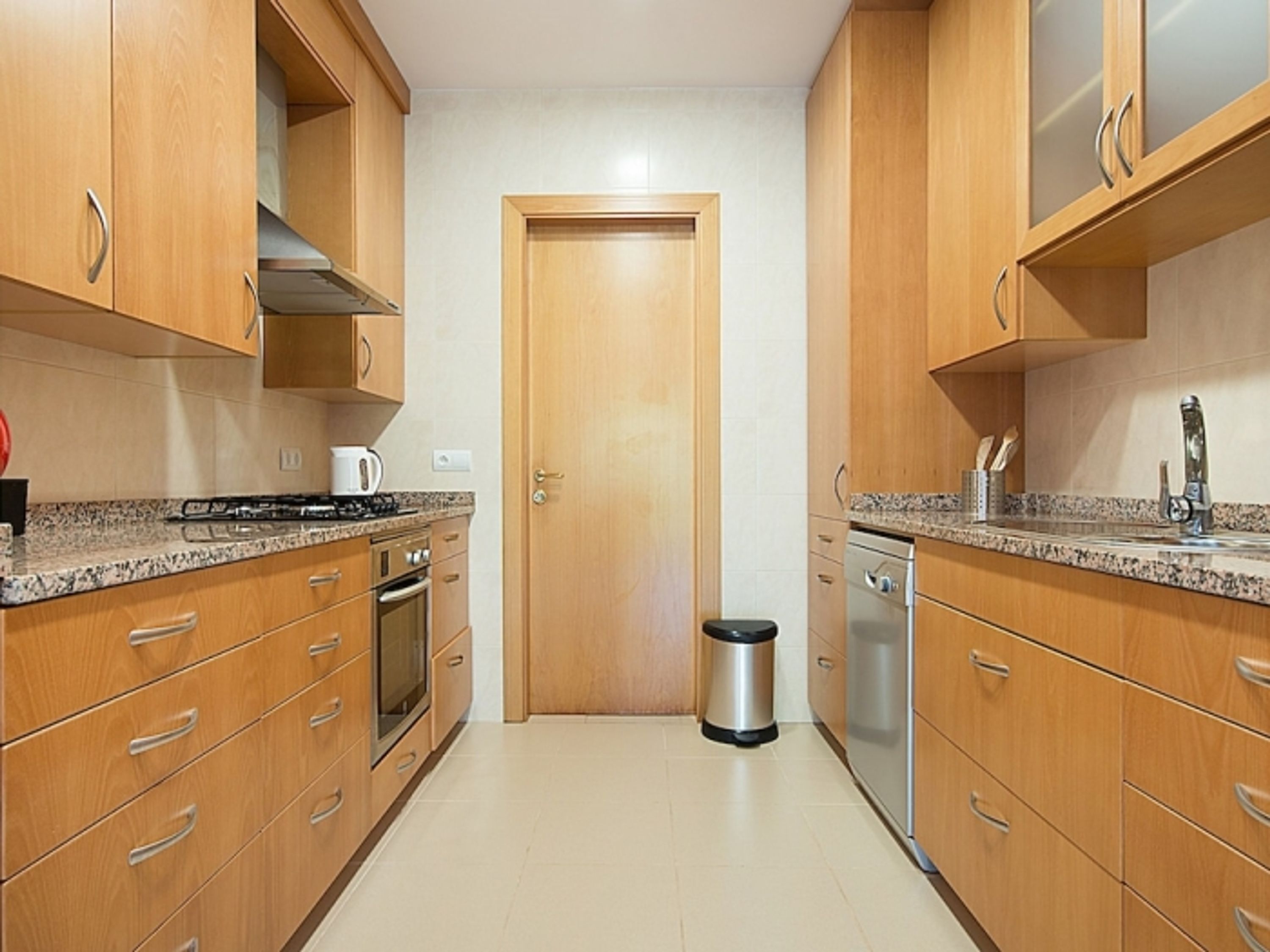 Una cocina con armarios de madera, una estufa de acero inoxidable y un cubo de basura.