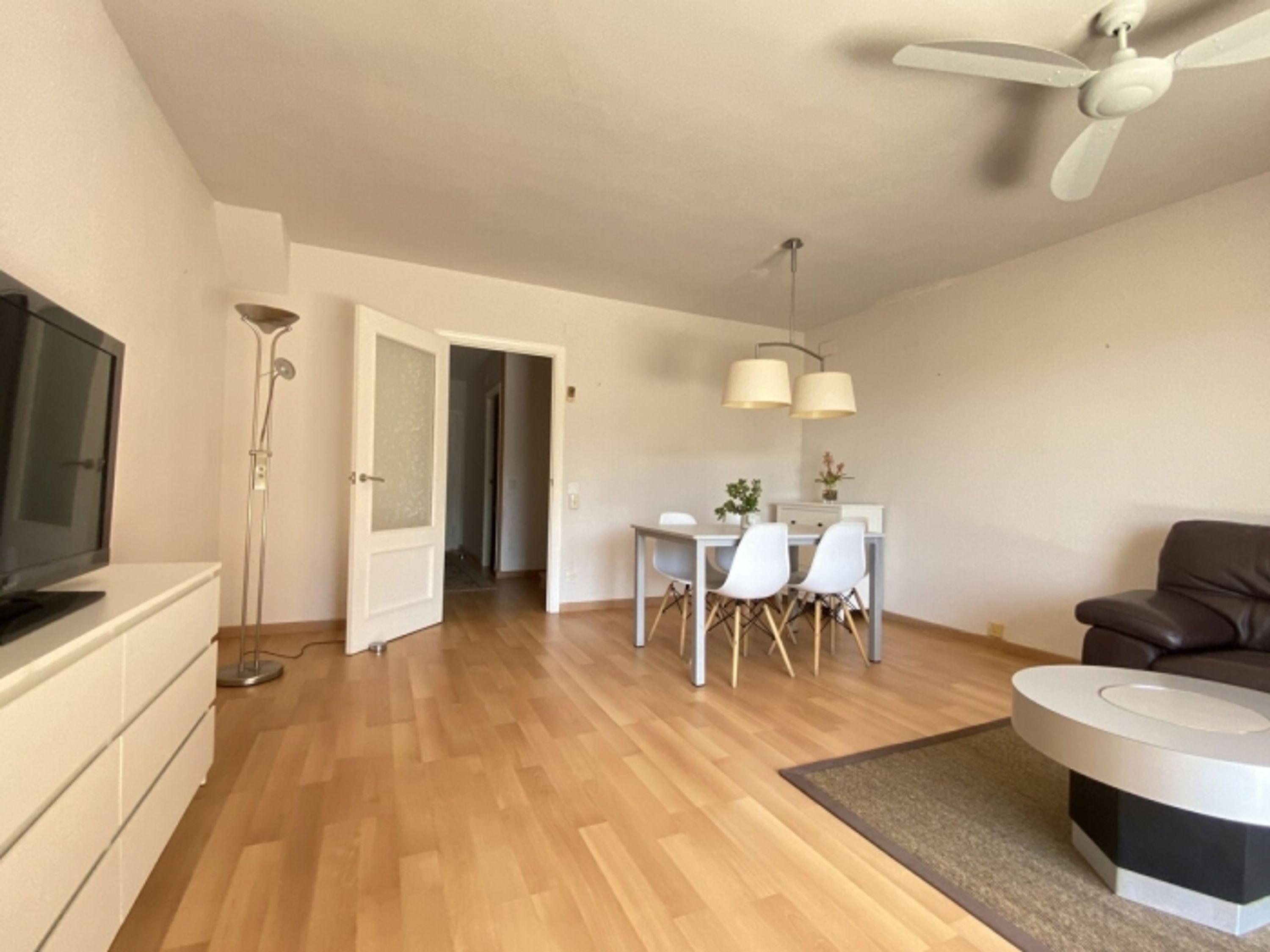 Un salon moderne doté d’un téléviseur à écran plat, d’un ventilateur de plafond, d’un coin repas avec une table et des chaises, et d’un canapé en cuir marron.