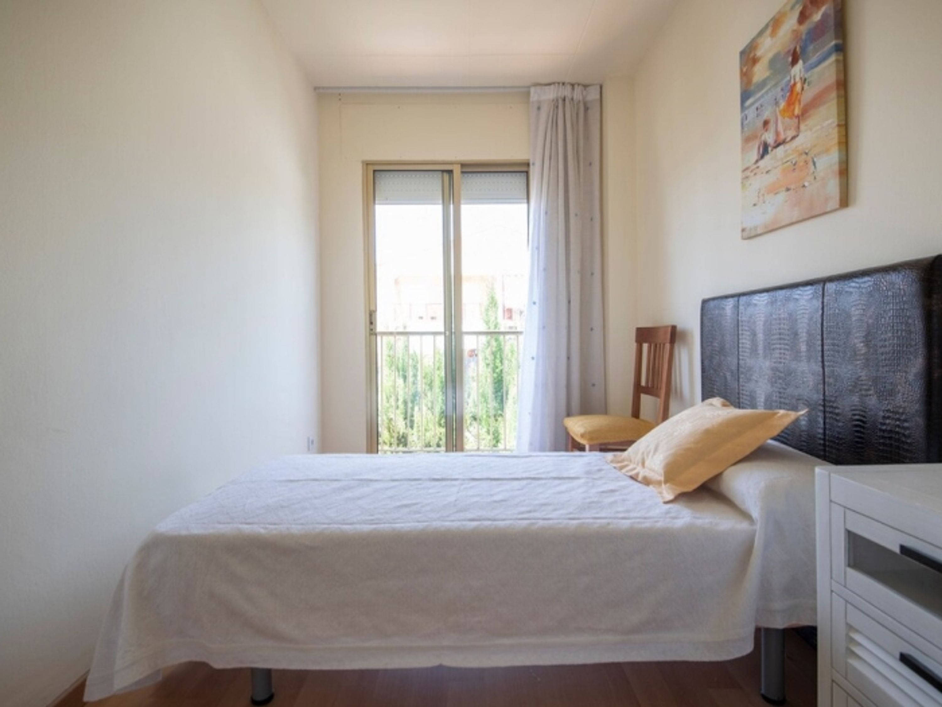 Ein Schlafzimmer mit einem Bett, einem Sessel, einer Kommode und einem Bild an der Wand.