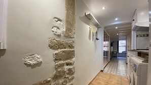 A narrow hallway with a stone wall on one side and a tiled floor. There is a washing machine on the right side. - Th143 Acogedor Estudio en Parte Alta (Tarragona)