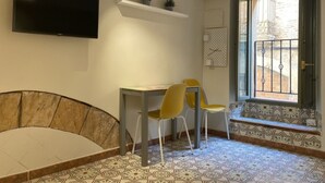 A room with a TV mounted on the wall, a small table with two chairs, a bench, and a window with a view of the outside. - Th143 Acogedor Estudio en Parte Alta (Tarragona)