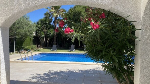 A swimming pool with a clear blue water, surrounded by lush greenery and red flowers, under a white archway. - Th11 Villa in Cambrils con Piscina (Cambrils)