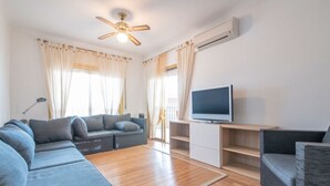 Una sala de estar moderna con un sofá modular, un televisor de pantalla plana sobre un soporte de madera y un ventilador de techo.