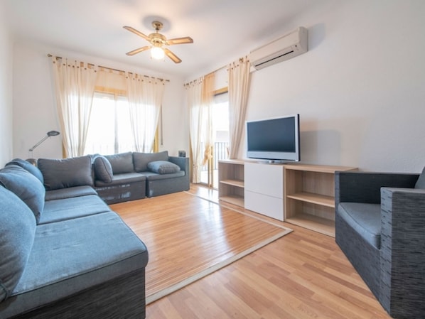 Ein modernes Wohnzimmer mit einem Ecksofa, einem Flachbildfernseher auf einem Holzboden und einem Deckenventilator.