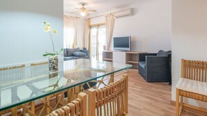 Una sala de estar moderna con una mesa de comedor de cristal, sillas de madera, un sofá y una televisión.