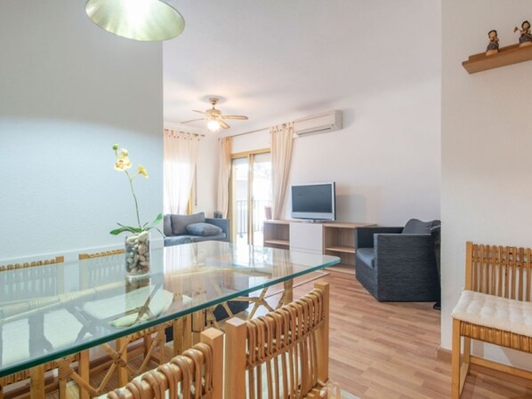 Ein modernes Wohnzimmer mit einem Glastisch, Holzstühlen, einer Couch und einem Fernseher.