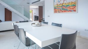 Een ruime eethoek met een witte tafel, zwarte stoelen, een trap en een kleurrijk schilderij aan de muur.