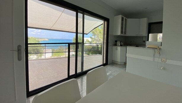 A modern kitchen with white cabinets and a large sliding glass door leading to a balcony with a view of the sea.