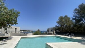 A rectangular swimming pool with clear blue water, surrounded by a tiled deck. There are lounge chairs along the poolside.