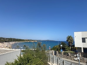 A coastal view with a beach, a clear sky, and a modern building with a balcony.