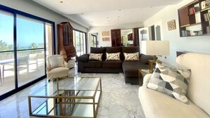 A spacious living room with a large window, a dark brown sofa set, a beige armchair, and a glass coffee table.