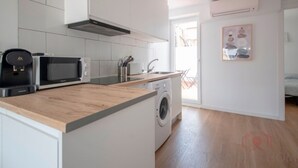 A modern kitchen with white cabinets, a wooden countertop, a built-in washing machine, a microwave, and a coffee maker.