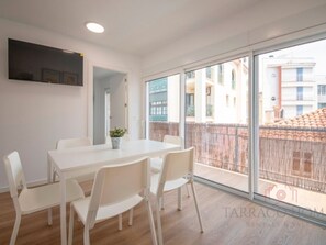 Un appartement moderne doté d’un grand balcon, de meubles blancs et offrant une vue sur les immeubles voisins.