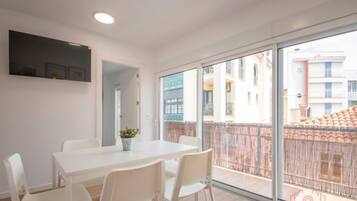 Un apartamento moderno con un balcón grande, muebles blancos y vistas a edificios vecinos.