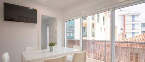 Eine moderne Wohnung mit großem Balkon, weißen Möbeln und Blick auf benachbarte Gebäude.