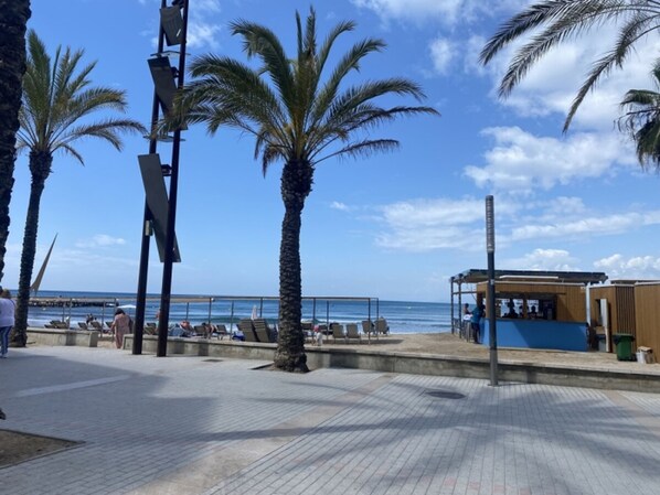 Un paseo marítimo frente a la playa con palmeras, una estructura de madera y vistas al océano.