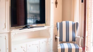 Una habitación con un televisor montado en un mueble blanco, un sillón a rayas y una mesita.