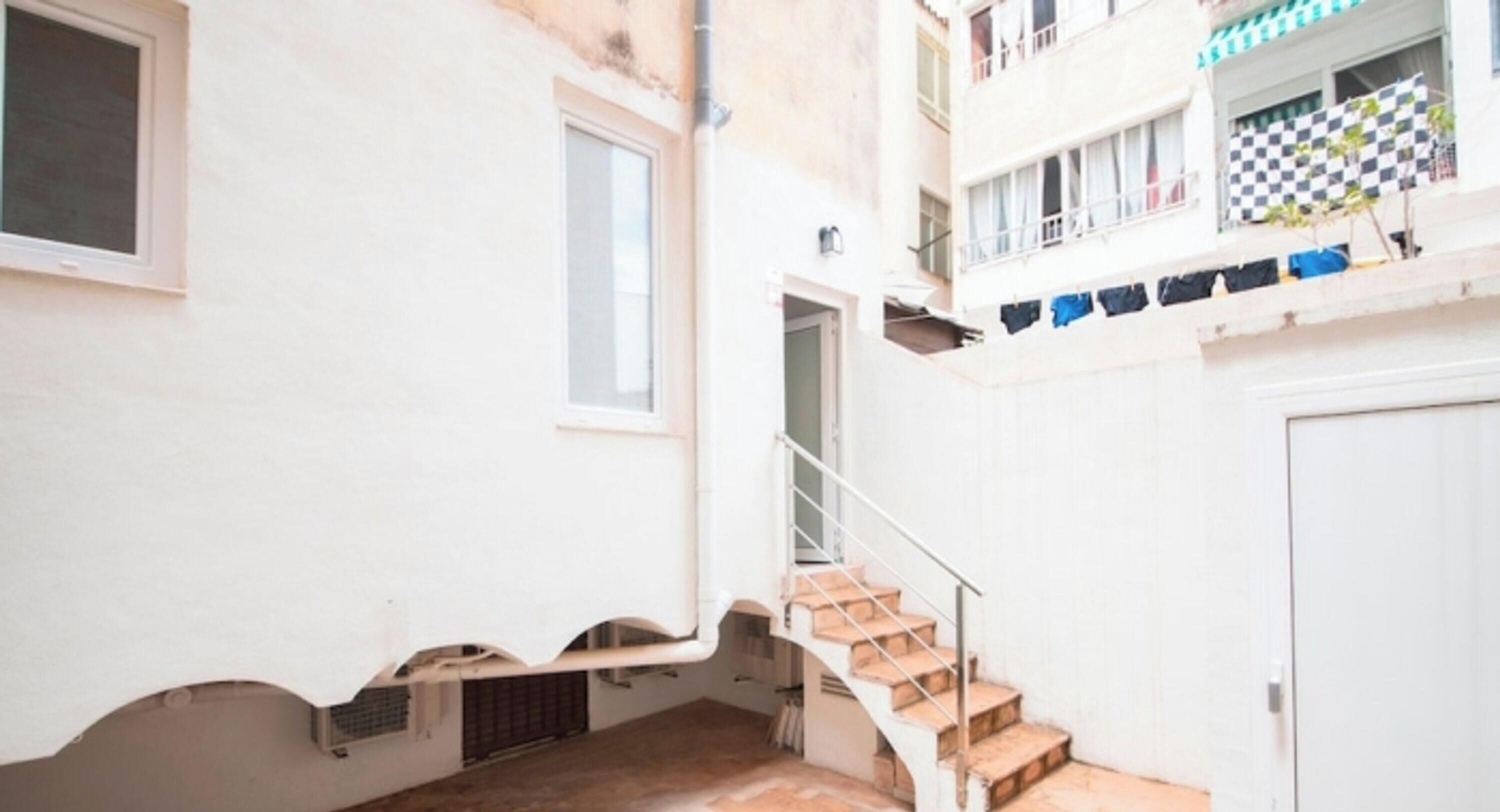 Eine enge Treppe führt zu einem Balkon im zweiten Stock, an der Brüstung hängt ein kariertes Tuch.