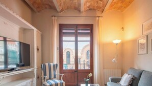 Un salón con televisor, un sillón a rayas, un sofá gris, una puerta de madera con vistas y una lámpara de pared.