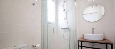 A modern bathroom with a glass-enclosed shower, a toilet, and a sink with a mirror above.