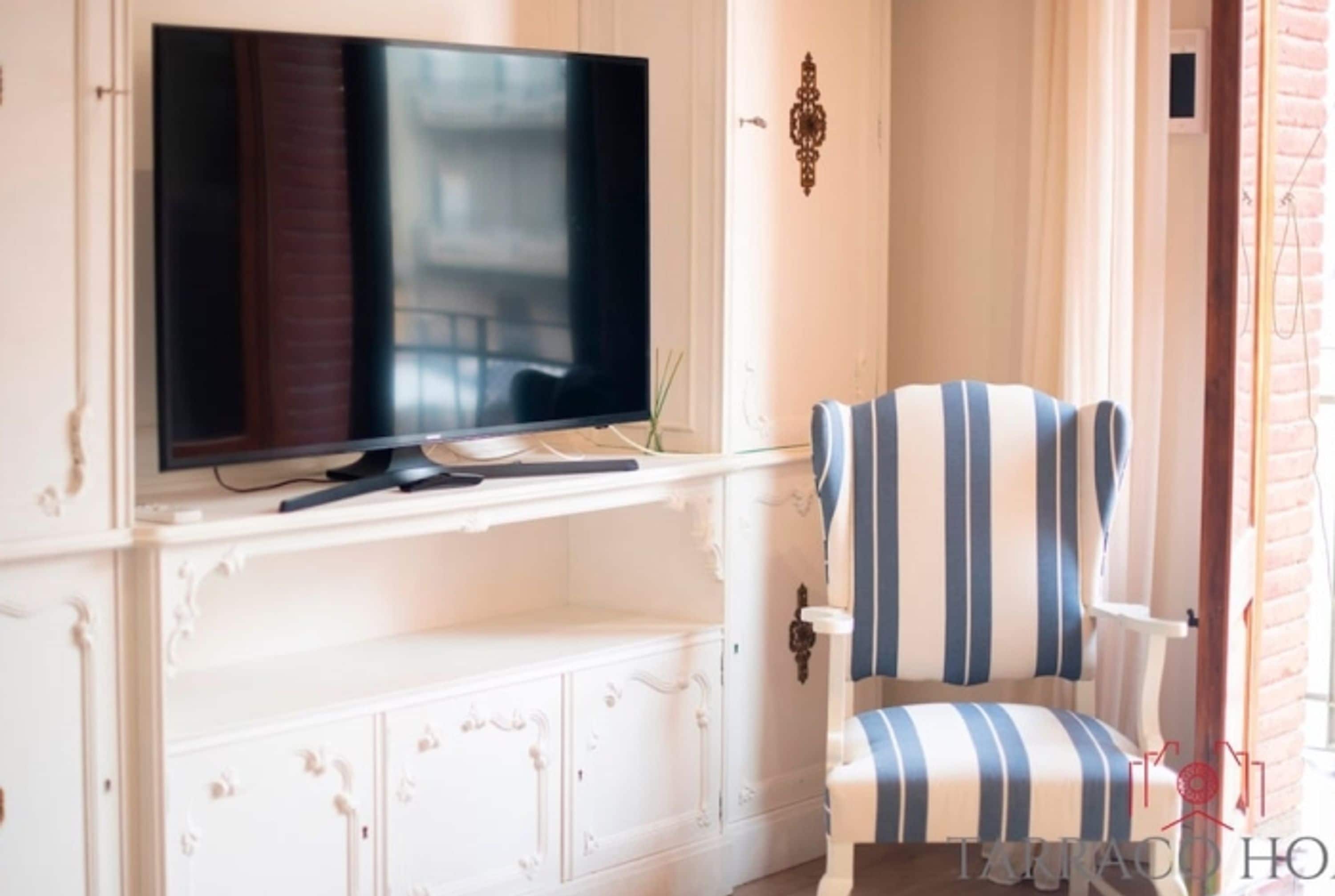 A room with a television mounted on a white cabinet, a striped armchair, and a small table.